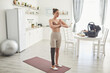 Full length portrait of active young woman with disability meditating during yoga workout at home with baby in background, copy space