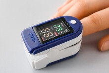 Hand with pulse oximeter on grey background