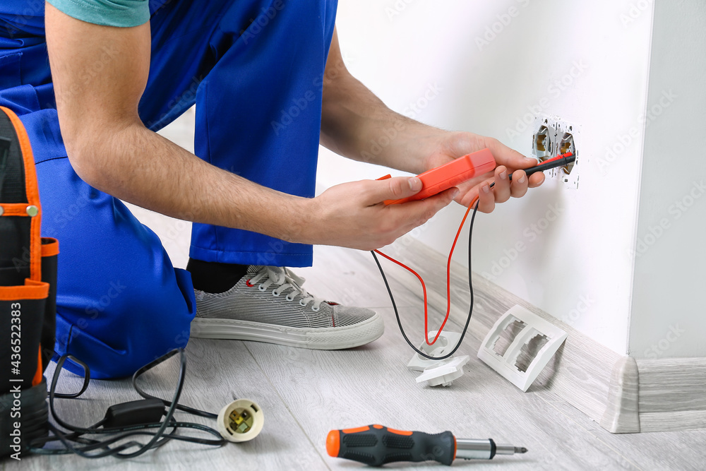 Young electrician measuring voltage of socket in room, closeup