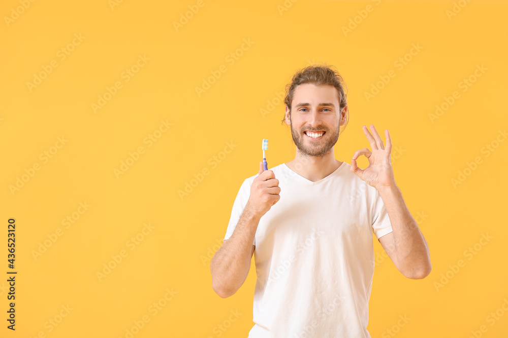 Young man brushing teeth and showing OK on color background