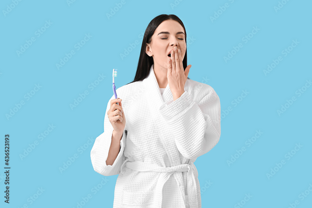 Tired young woman with tooth brush on color background