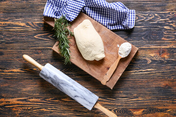 Board with fresh dough, flour, rosemary and rolling pin on wooden background