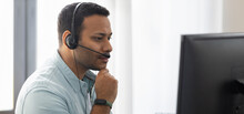 Focused Young Indian Man With In Headphones Working At Laptop At Home Office, Call Center Employee, Advises Clients Online, Support Operator, Copy Space