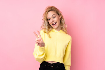 Poster - Young blonde woman wearing a sweatshirt isolated on pink background smiling and showing victory sign