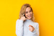 © luismolinero - Young blonde woman isolated on yellow background making phone gesture and pointing front