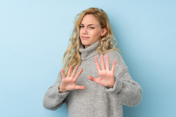 Canvas Print - Young blonde woman wearing a sweater isolated on blue background nervous stretching hands to the front