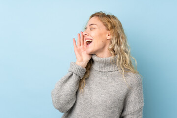 Canvas Print - Young blonde woman wearing a sweater isolated on blue background shouting with mouth wide open to the lateral