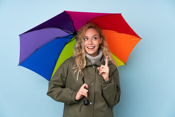 Poster - Young blonde woman holding an umbrella isolated on blue background intending to realizes the solution while lifting a finger up