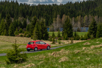 Red fast car in spring sunrise forest on wet black road after rain