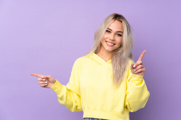 Teenager girl wearing a yellow sweatshirt over isolated purple background pointing finger to the laterals and happy