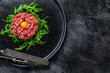 Beef tartar with a quail egg served on a black stone plate.. Black background. Top view. Copy space