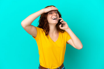 Teenager reddish woman using mobile phone isolated on blue background smiling a lot