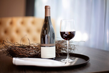 A bottle of red wine and a full glass on a tray stand on a table in the restaurant. Empty label template. Close-up