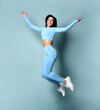 Sports and motivation. Full length portrait of an excited young female athlete with a perfect figure bouncing on a blue background. Woman in stylish sportswear jumps near the free space for text.