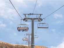 Open Cable Car, Chairlift With Empty Seats On The Background Of A Blue Sky With Clouds, A View From Below Of The Ascent. The Concept Of A Dangerous, Risky Lift.