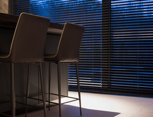 Leinwandbilder - Wood blinds black color on large windows in the interior. Next to the window is a table with chairs. The park is visible through the blinds. Motorized venetian wooden blinds closeup. Selective focus. 