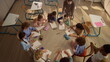 © stockbusters - smiling schoolteacher helping students. Scool kids sitting at round desk