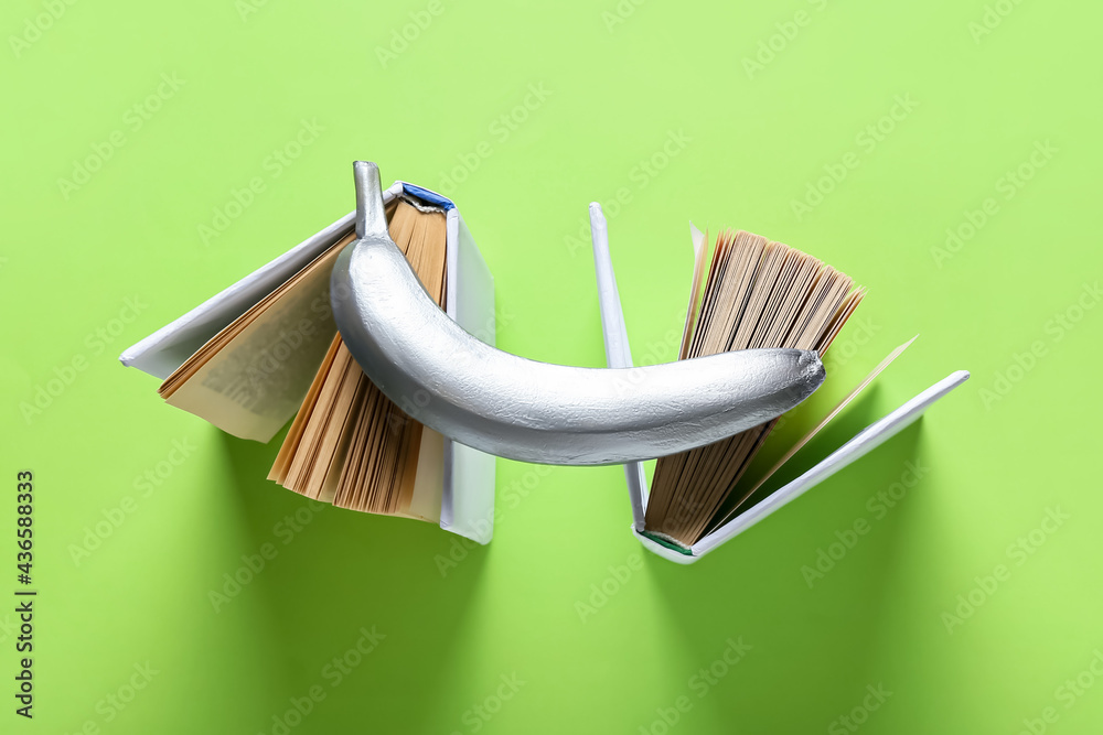 Creative composition with painted banana and books on color background