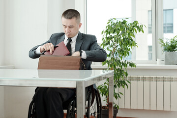 Poster - Businessman in wheelchair putting notebook into briefcase before leaving office