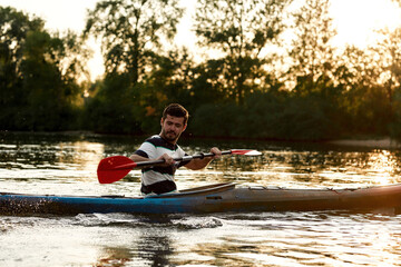 Wall Mural - Cheerful young caucasian man having fun while kayaking on a lake surrounded by nature