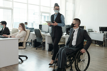 two colleagues in protective masks interacting while moving along open space office