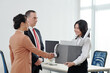 © DragonImages - Businesswoman with box of belongings shaking hands of her new colleagues