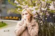 © Angelov - Young pretty woman sneezing in front of blooming tree. Spring allergy concept