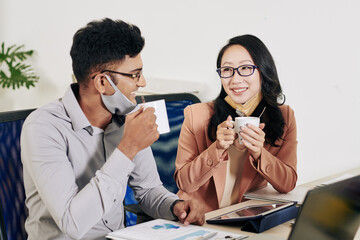 Wall Mural - Cheerful young business people drinking coffee and discussing project developement at office table