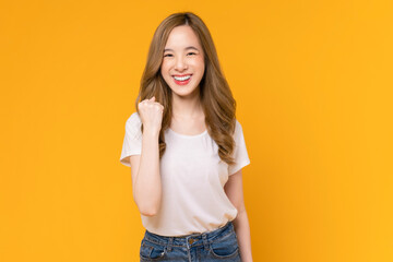 Cheerful beautiful Asian woman in a white t-shirt raises arms and fists clenched with shows strong powerful, celebrating victory expressing success.