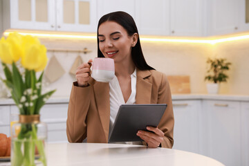 Canvas Print - Young woman with tablet having breakfast in kitchen. Morning routine