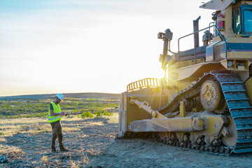 Wall Mural - Construction inspector wearing safety helmet and reflective vest taking notes during an inspection of heavy machinery on a road construction site