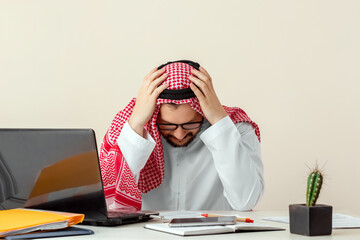 Wall Mural - An Arab man, a businessman, a sheikh works at a laptop. Investments, business, work via the Internet, online contracts.