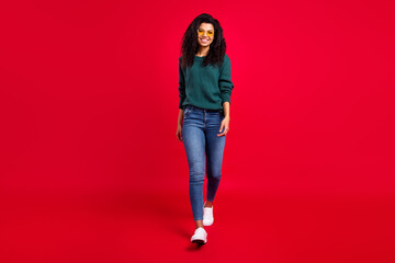 Wall Mural - Full size photo of optimistic wavy hairdo lady go wear spectacles sweater jeans sneakers isolated on red color background