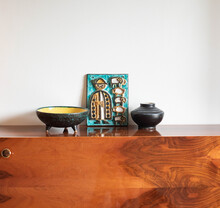 Mid-century Modern Ceramic Bowl With Small Feet, A Vase And A Wall Plaque On A Wooden Sideboard