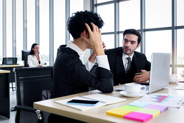 Businessman and businesswoman using a laptop together, seriously discussing about project work while sitting at office working desk. businesspeople with workplace stress