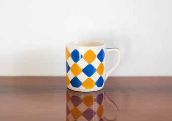 Mid-century modern ceramic mug with yellow and blue square pattern on a wooden table