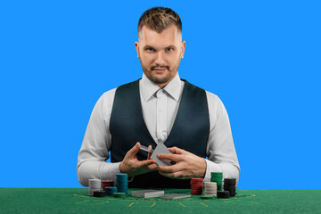 Male croupier at the casino at the table isolated on blue background. Casino concept, gambling, poker, chips on the green casino table.