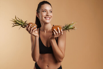 Wall Mural - Young brunette woman in swimsuit smiling while posing with pineapples