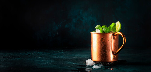 Moscow mule alcoholic cocktail in copper mug with lime, ginger beer, vodka and mint. Blue table, copper bar tools