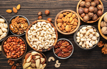 Wall Mural - Nuts in bowls. Walnuts, pistachios, pecans, macadamia, almonds and other. Healthy food snacks mix on wooden background, top view