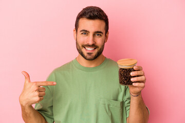 Wall Mural - Young caucasian man holding a coffee bottle isolated on pink background person pointing by hand to a shirt copy space, proud and confident