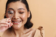 Young asian brunette woman smiling while using eyelash curler