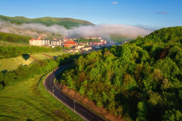 Scenic aerial view of the foggy Carpathian mountains, village and blue sky with clouds in morning light, summer rural landscape, outdoor travel background