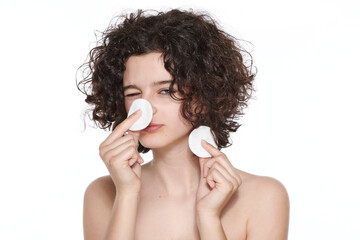 Teenager skincare. Beautiful teenage girl with gorgeous curly hair playing with make up removing cotton pads. Studio shot on white background. Beauty, skincare and puberty concept.