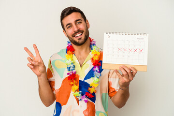 Wall Mural - Young caucasian woman waiting for his vacations holding a calendar isolated on white background joyful and carefree showing a peace symbol with fingers.