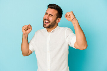 Young caucasian man isolated on blue background celebrating a special day, jumps and raise arms with energy.