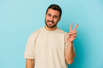 Young caucasian man isolated on blue background joyful and carefree showing a peace symbol with fingers.