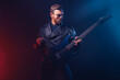 © zamuruev - Brutal bearded Heavy metal musician in leather jacket and sunglasses is playing electrical guitar. Shot in a studio on dark background with smoke