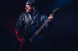 © zamuruev - Brutal bearded Heavy metal musician in leather jacket, cap and sunglasses is playing electrical guitar. Shot in a studio on dark background
