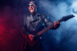 © zamuruev - Brutal bearded Heavy metal musician in leather jacket and sunglasses is playing electrical guitar. Shot in a studio on dark background with smoke